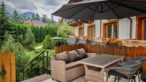 A patio with wicker furniture, a wooden table, and a large umbrella. - Skalny (Zakopane)