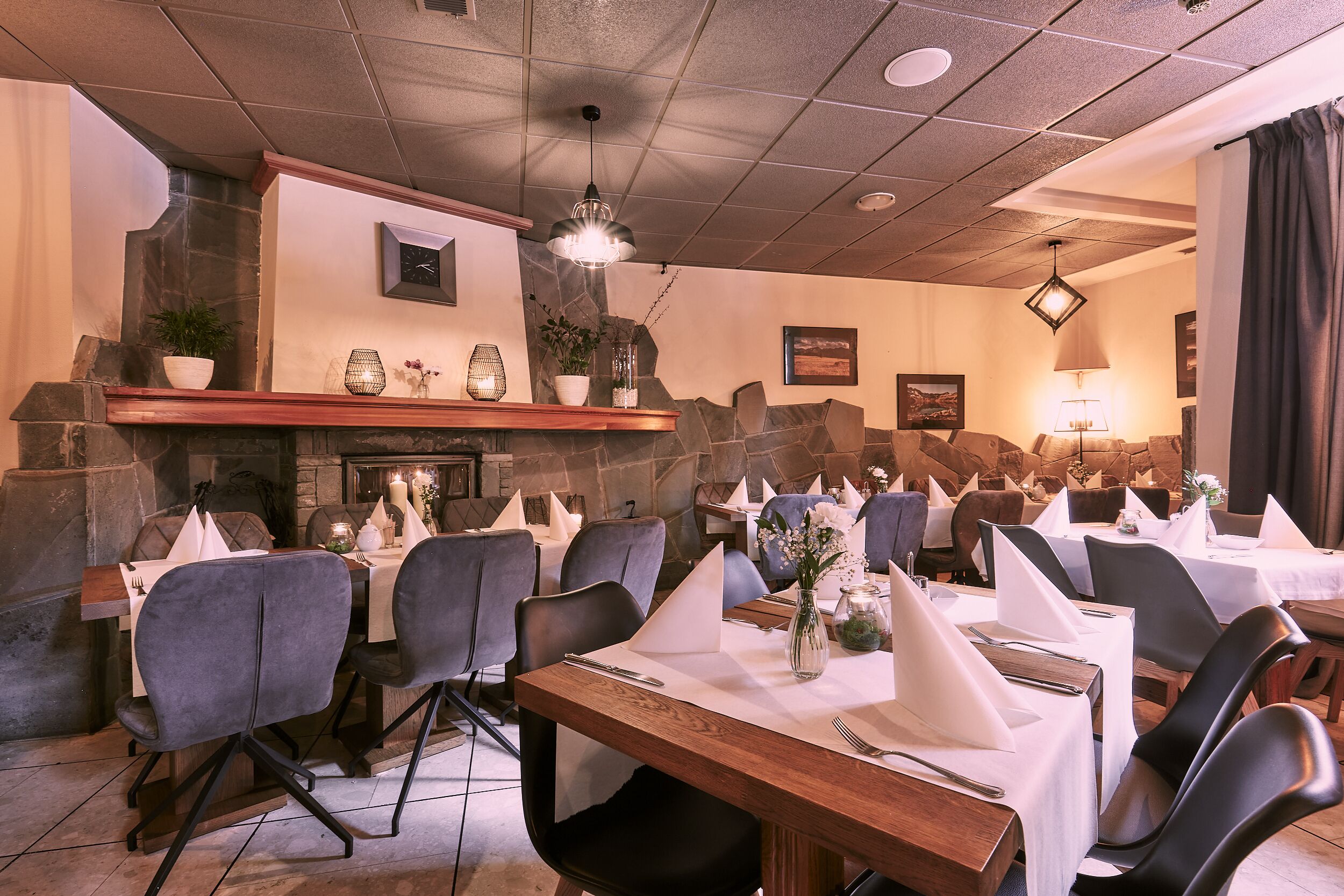 A restaurant with multiple tables set for dining, stone walls, and a fireplace.