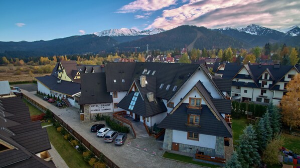 A hotel with a sign reading "HOTEL SKALNY CENTUM REKREACJI" surrounded by houses, a parking area, and mountains in the background. - Skalny (Zakopane)