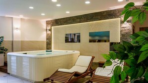 A spa area with a hot tub, wooden lounge chairs, and a stone wall with framed pictures. - Skalny (Zakopane)