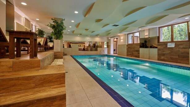 A swimming pool with a wooden deck and steps leading to it, surrounded by a modern interior with recessed lighting and wooden accents. - Skalny (Zakopane)