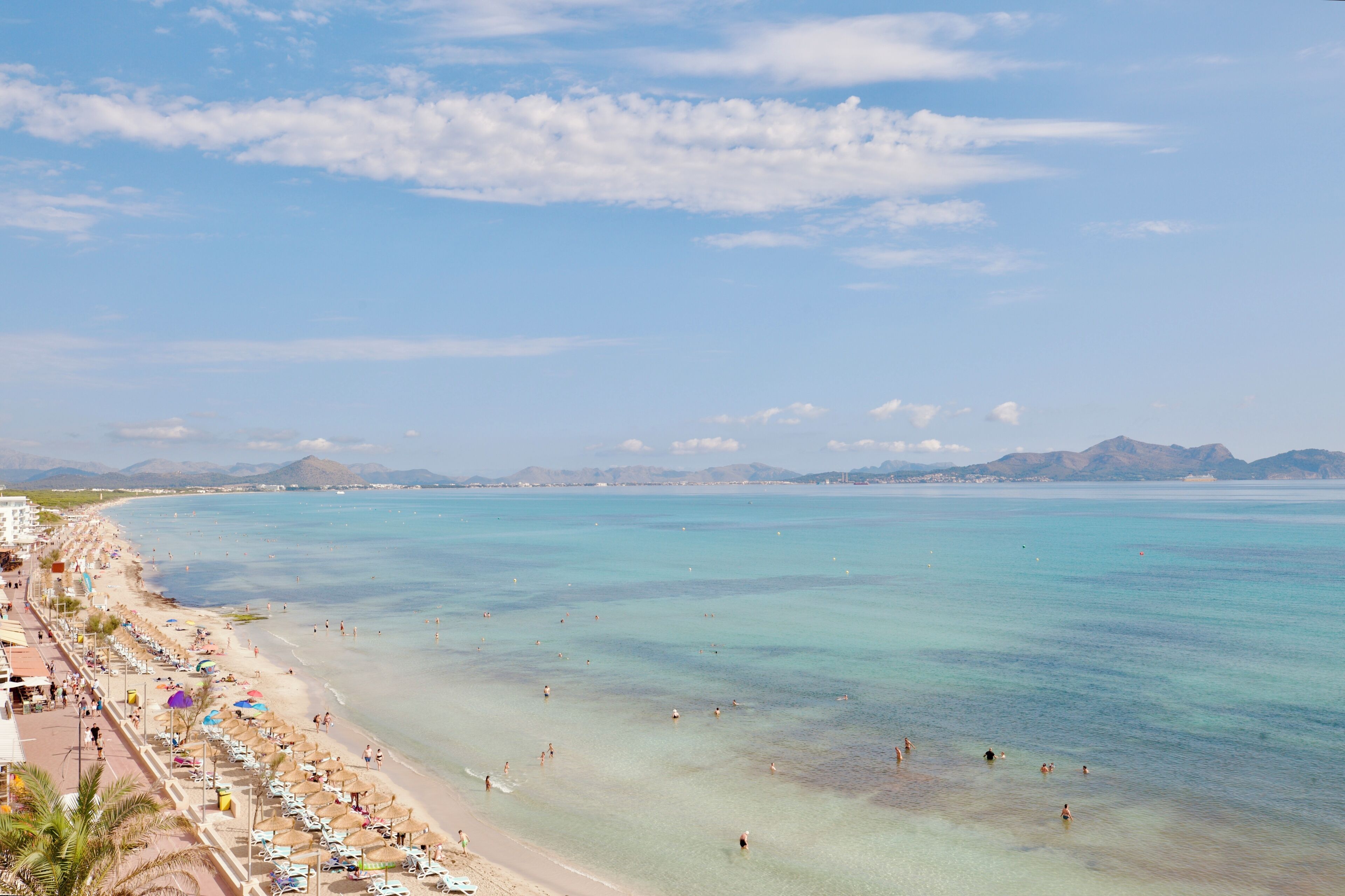 Una playa costera con aguas cristalinas, una orilla arenosa y montañas a lo lejos.