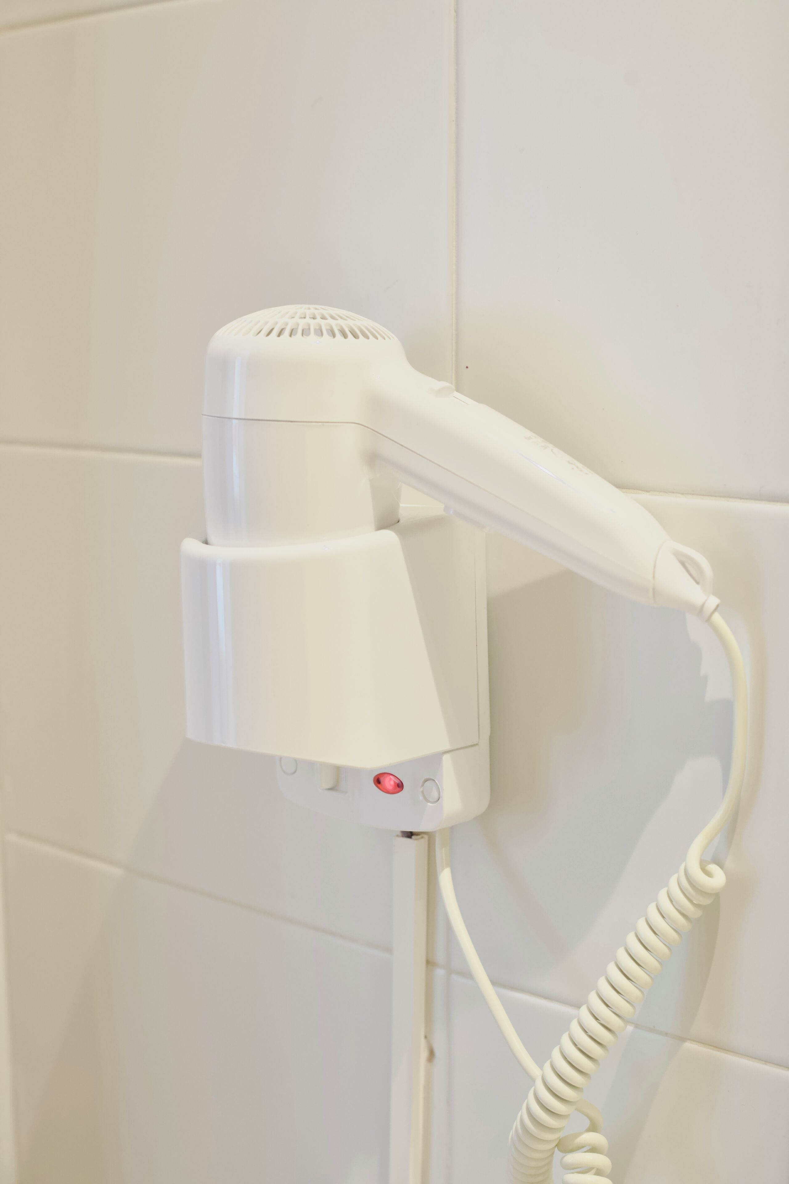Un secador de pelo blanco sujeto a la pared con un cable enrollado.
