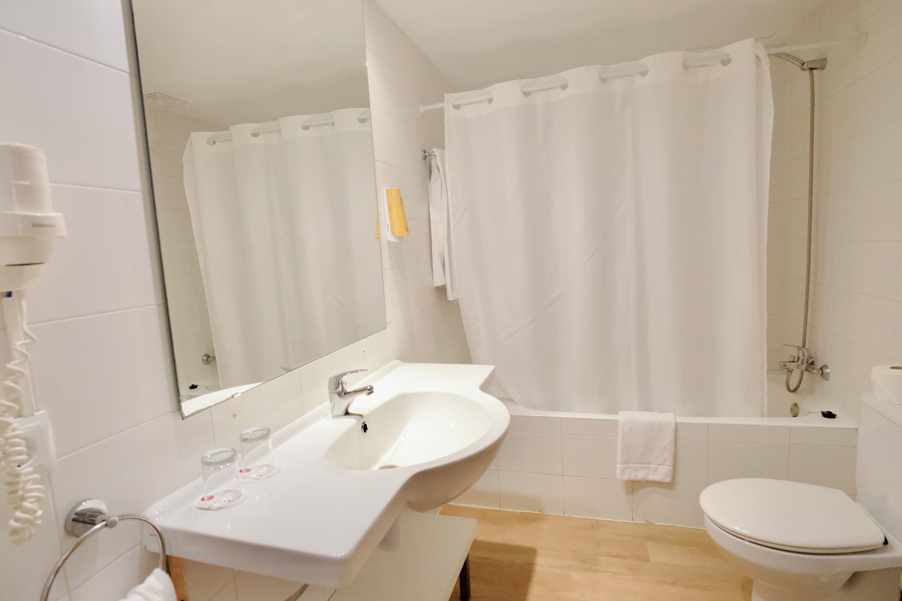 A bathroom with a sink, mirror, toilet, and shower curtain.
