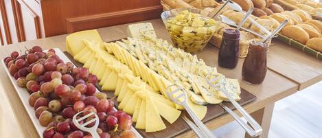 A buffet table with various cheeses, grapes, and bread.