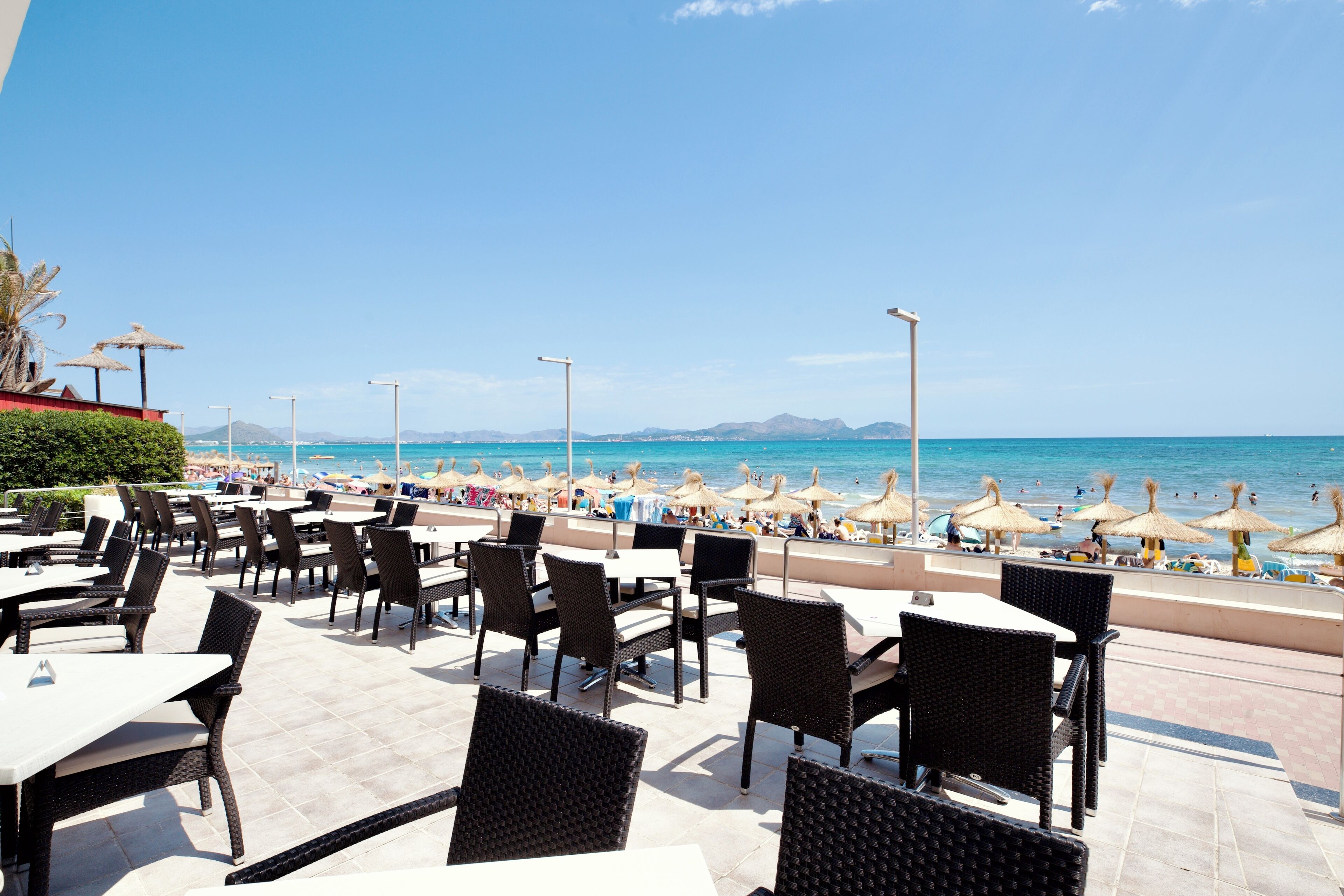 An outdoor dining area with tables and chairs, beach umbrellas, and a view of the beach and ocean.