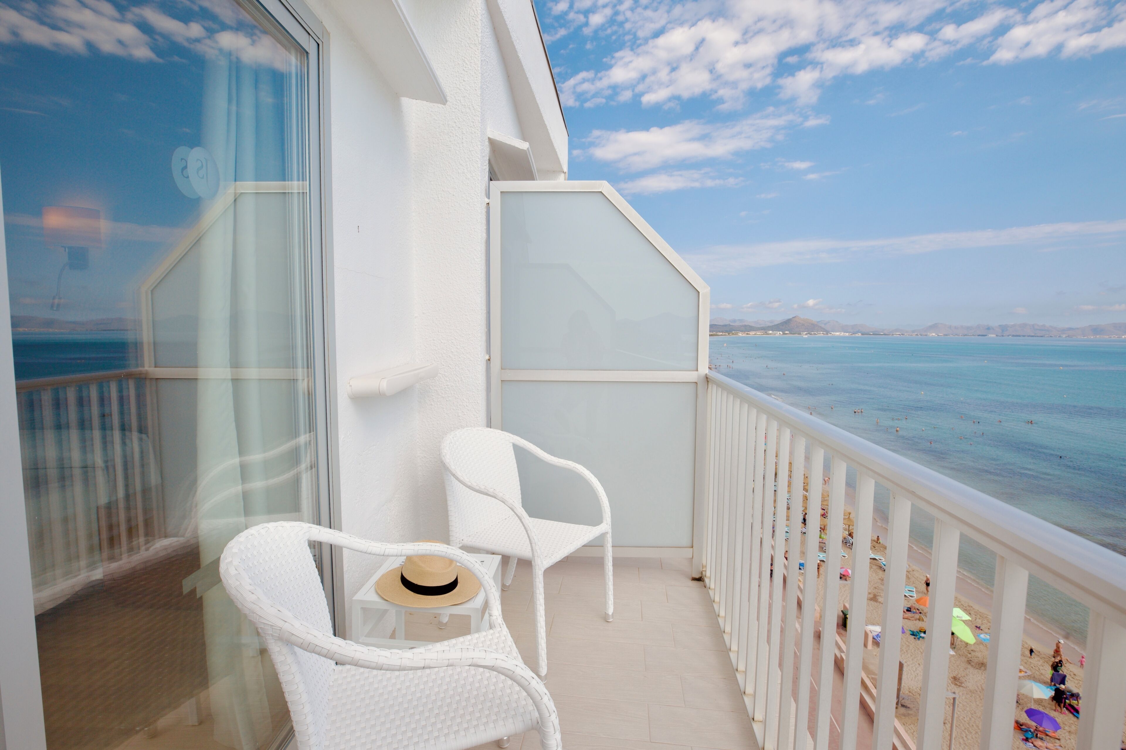 Een balkon met witte rieten meubels, uitzicht op zee en een heldere lucht.
