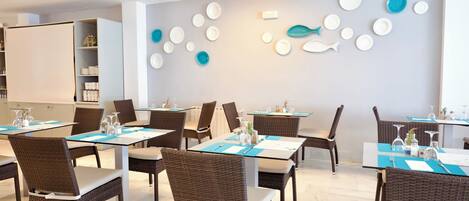 Een eetgedeelte met tafels voor vier personen, rieten stoelen en een muur met decoratieve borden.