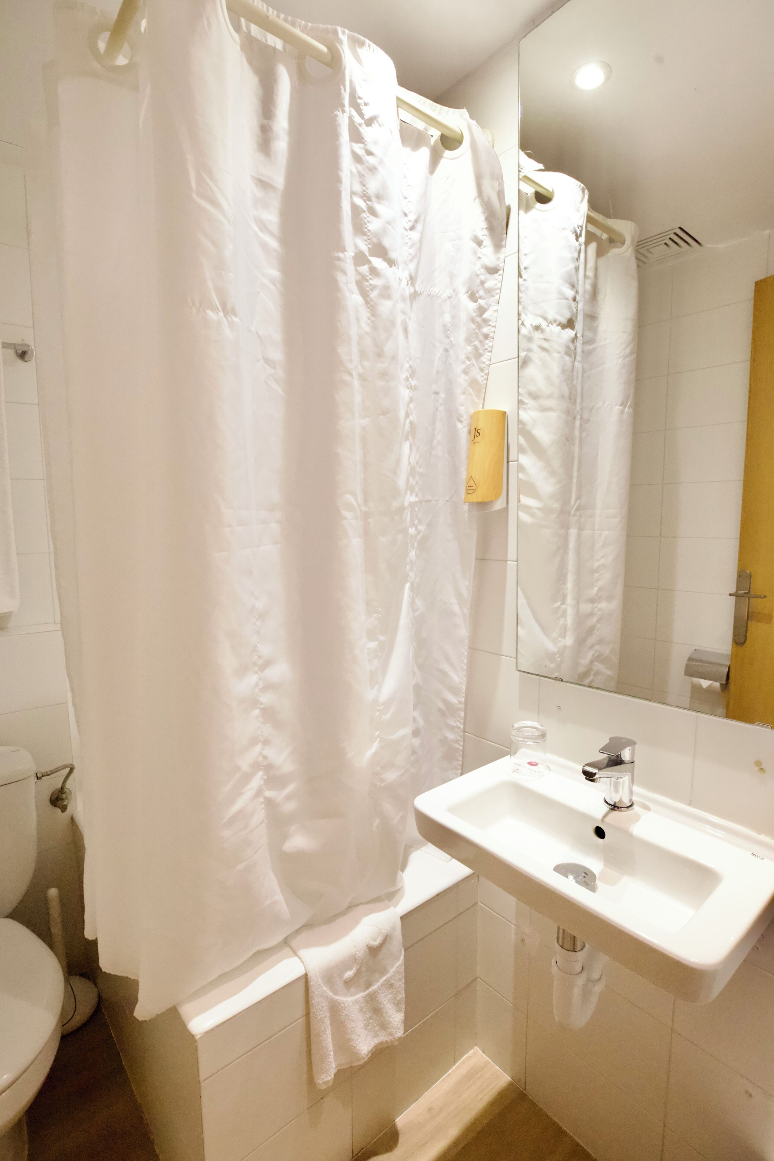 Une salle de bain avec un rideau de douche blanc, un lavabo et un miroir.