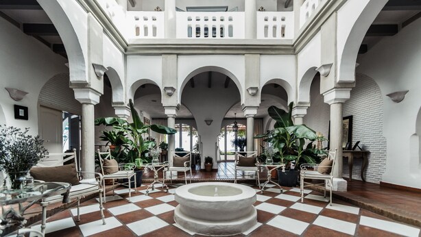Un vaste atrium doté d’un sol à carreaux, de colonnes blanches et d’espaces aménagés avec des plantes en pot.