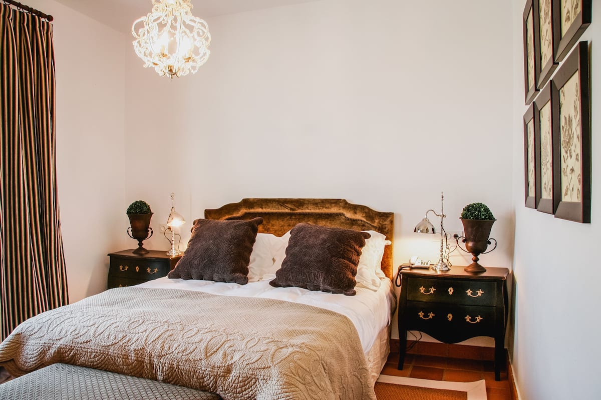 A neatly made bed with a wooden headboard, two bedside tables with lamps, and a chandelier above.