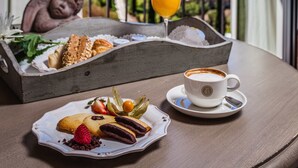 Un balcon avec une table préparée pour le petit-déjeuner, comprenant des viennoiseries, une tasse de café et un verre de jus d’orange, offrant une vue panoramique sur des collines.