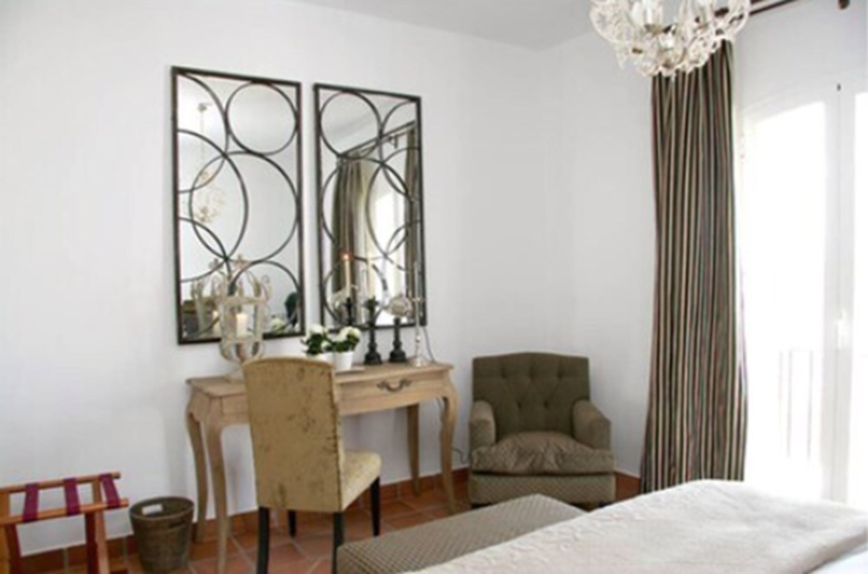 A bedroom with a bed, a desk with a chair, a large mirror, and a window with curtains.