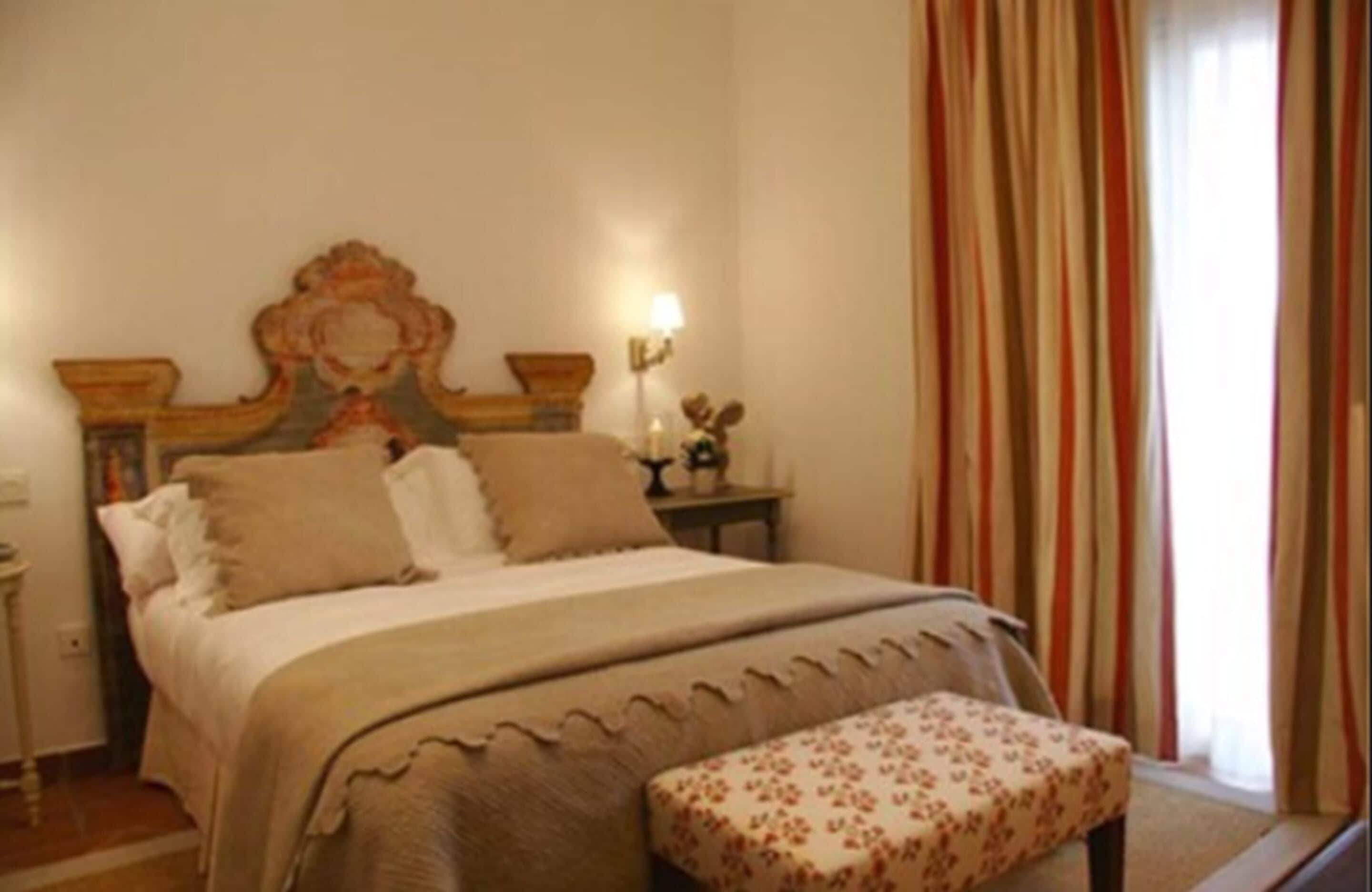 Une chambre à coucher avec un lit, une table de chevet, une lampe et une fenêtre avec des rideaux.