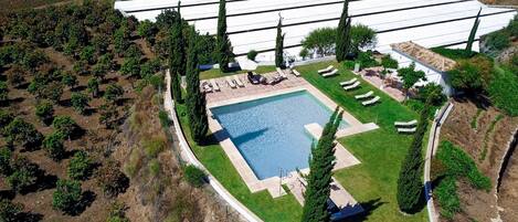 Vue aérienne d’une propriété dotée d’une piscine, de chaises longues et d’un vignoble.