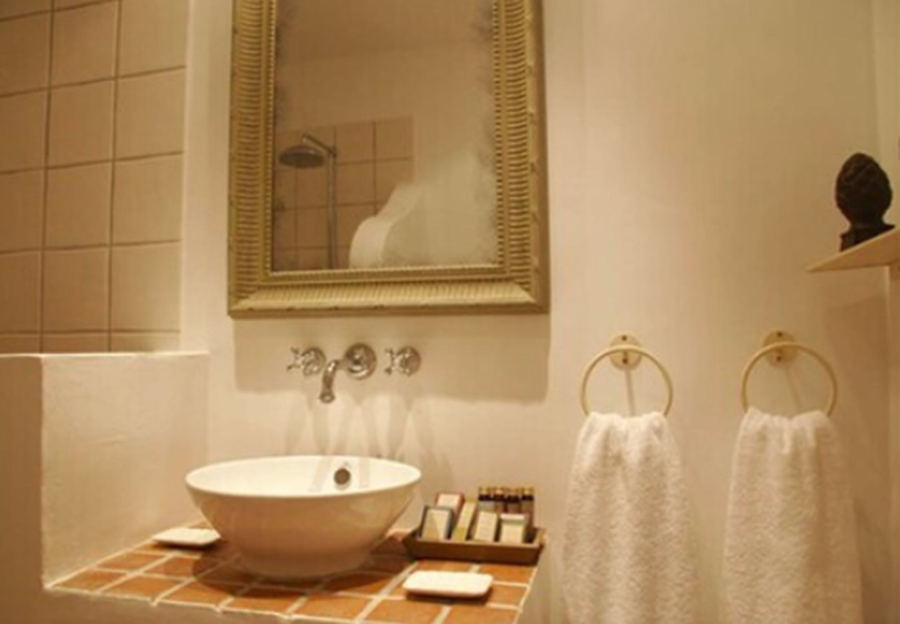 Un baño con un espejo grande, un lavabo blanco y dos toallas colgadas en aros.