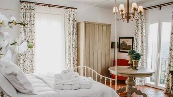 Un dormitorio con cama, cortinas blancas, armario de madera, candelabro y una mesa con plantas en macetas.