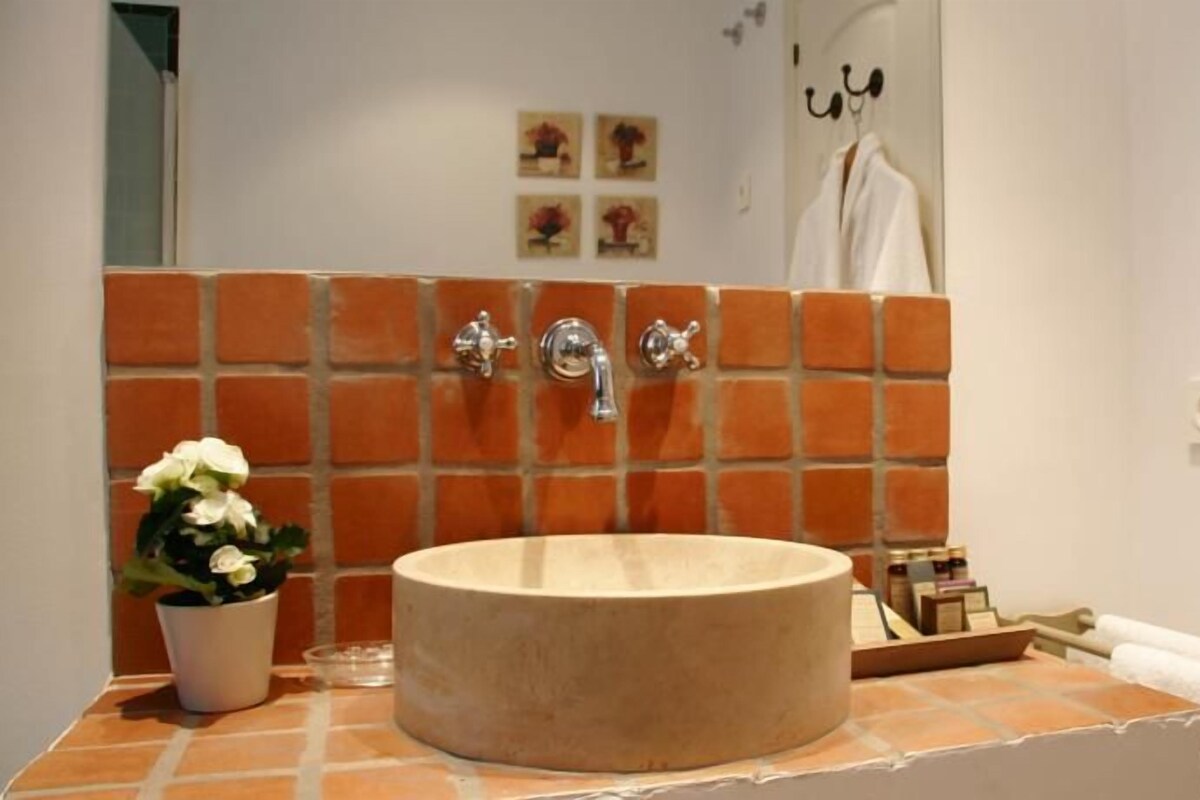 Un baño con un lavamanos redondo, una planta en maceta, un perchero para toallas y un espejo.