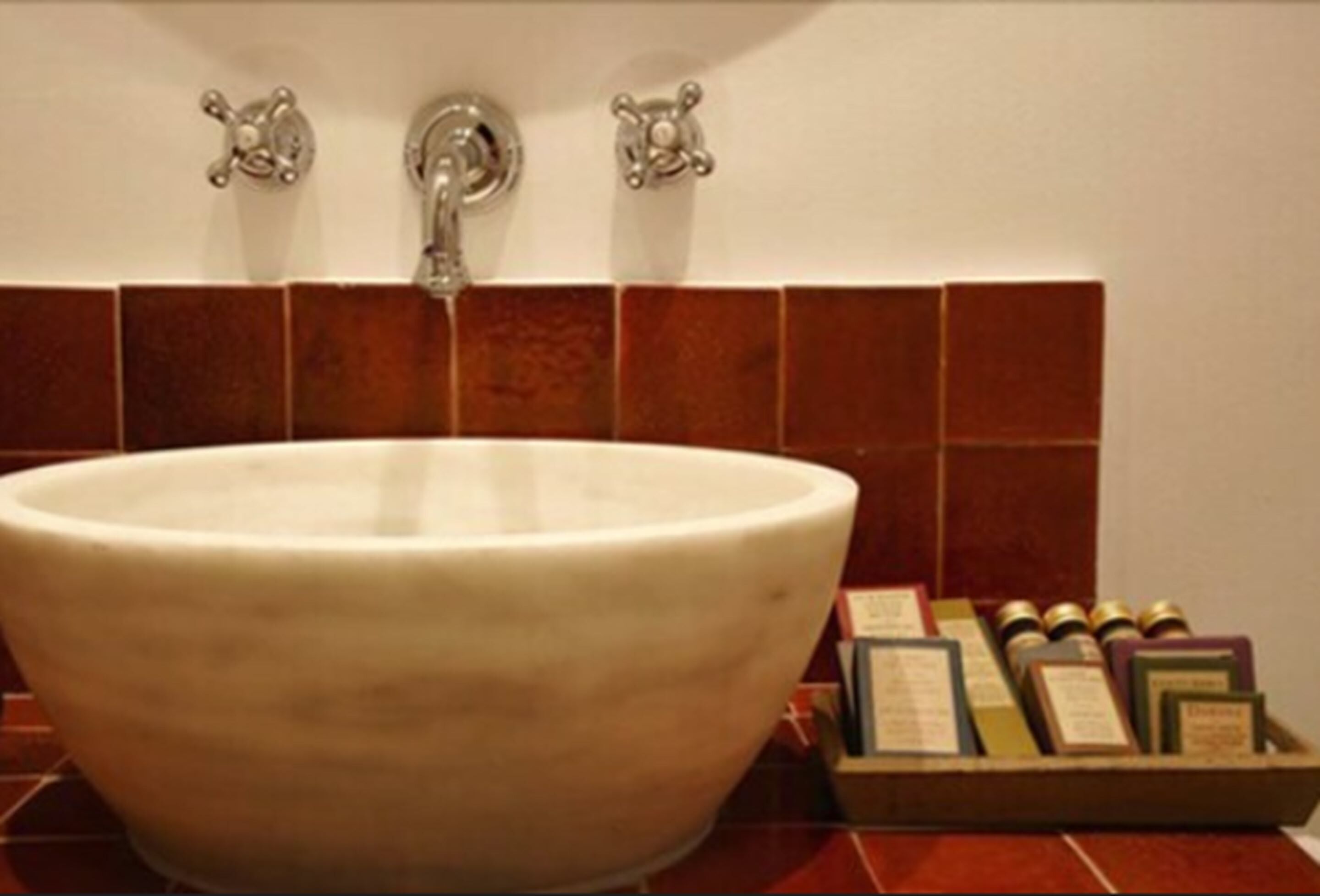 Un lavamanos grande y blanco con un solo grifo en un baño con paredes de azulejos rojos.