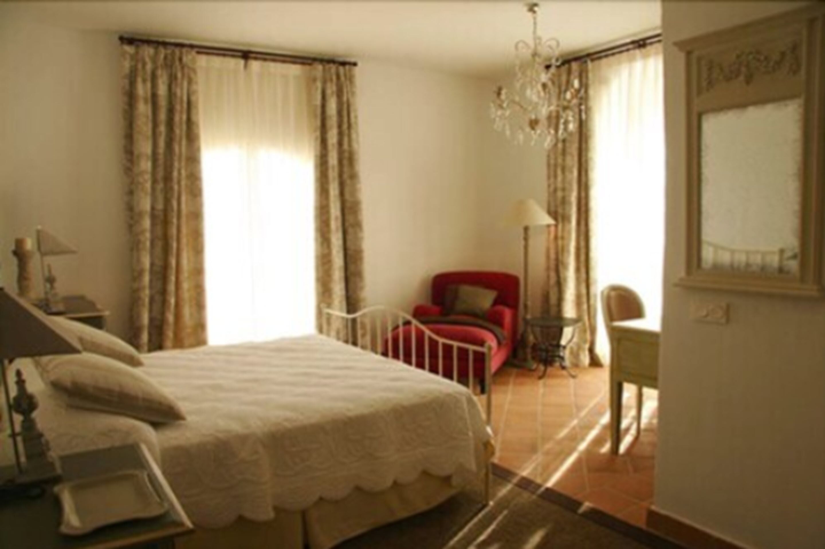 A bedroom with a bed, a chair, a desk, and a chandelier.