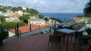 Eine Terrasse mit Sitzgelegenheit im Freien, Blick auf das Meer und Gebäude im Hintergrund.
