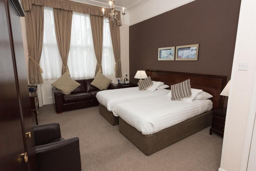 A hotel room with two beds, a sofa, a chandelier, and framed pictures on the wall.