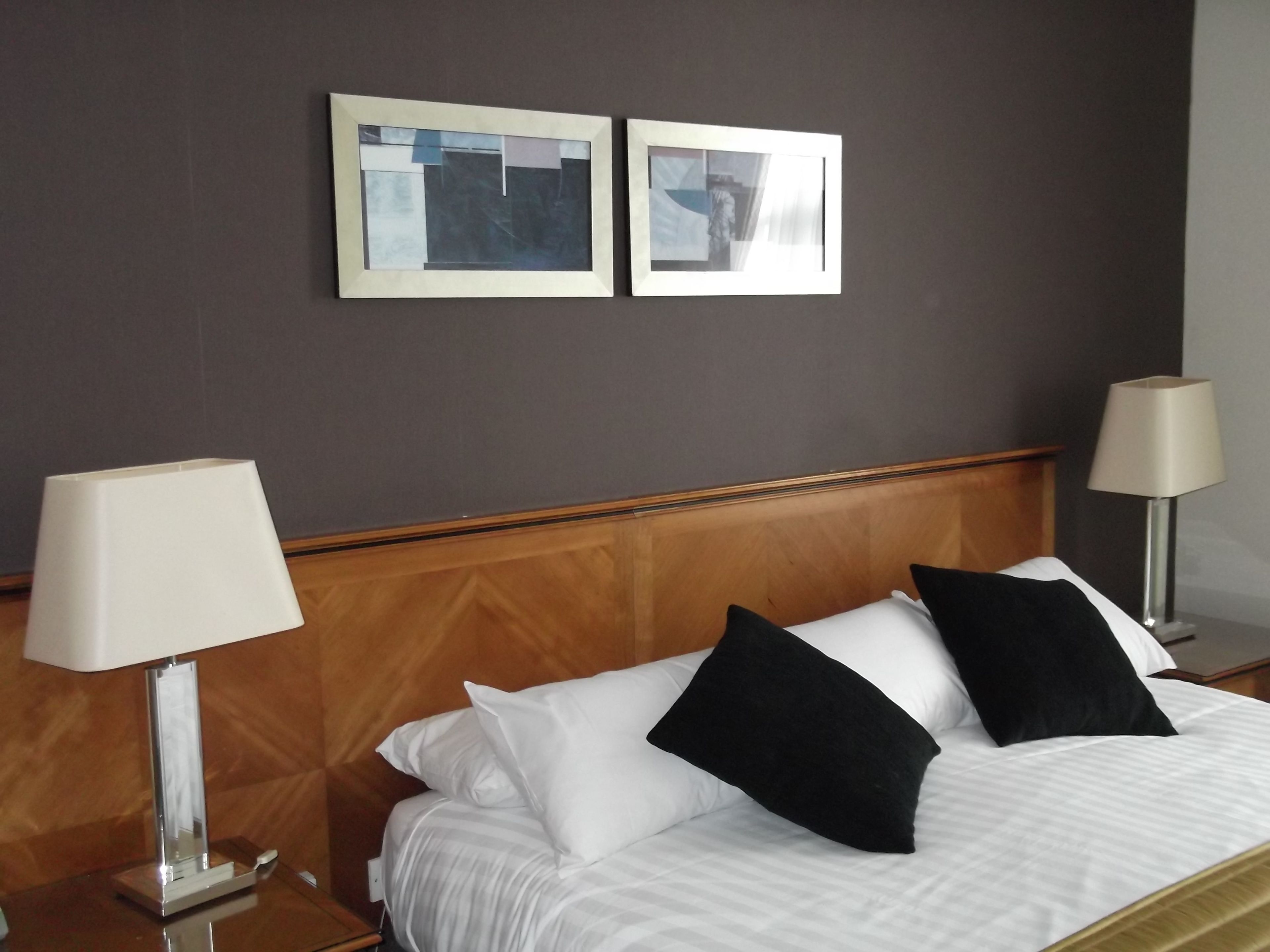 A hotel room with a bed, two bedside lamps, and two framed pictures on the wall.