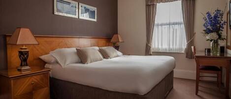 A hotel room with a large bed, two bedside tables, a desk, and a window with curtains.