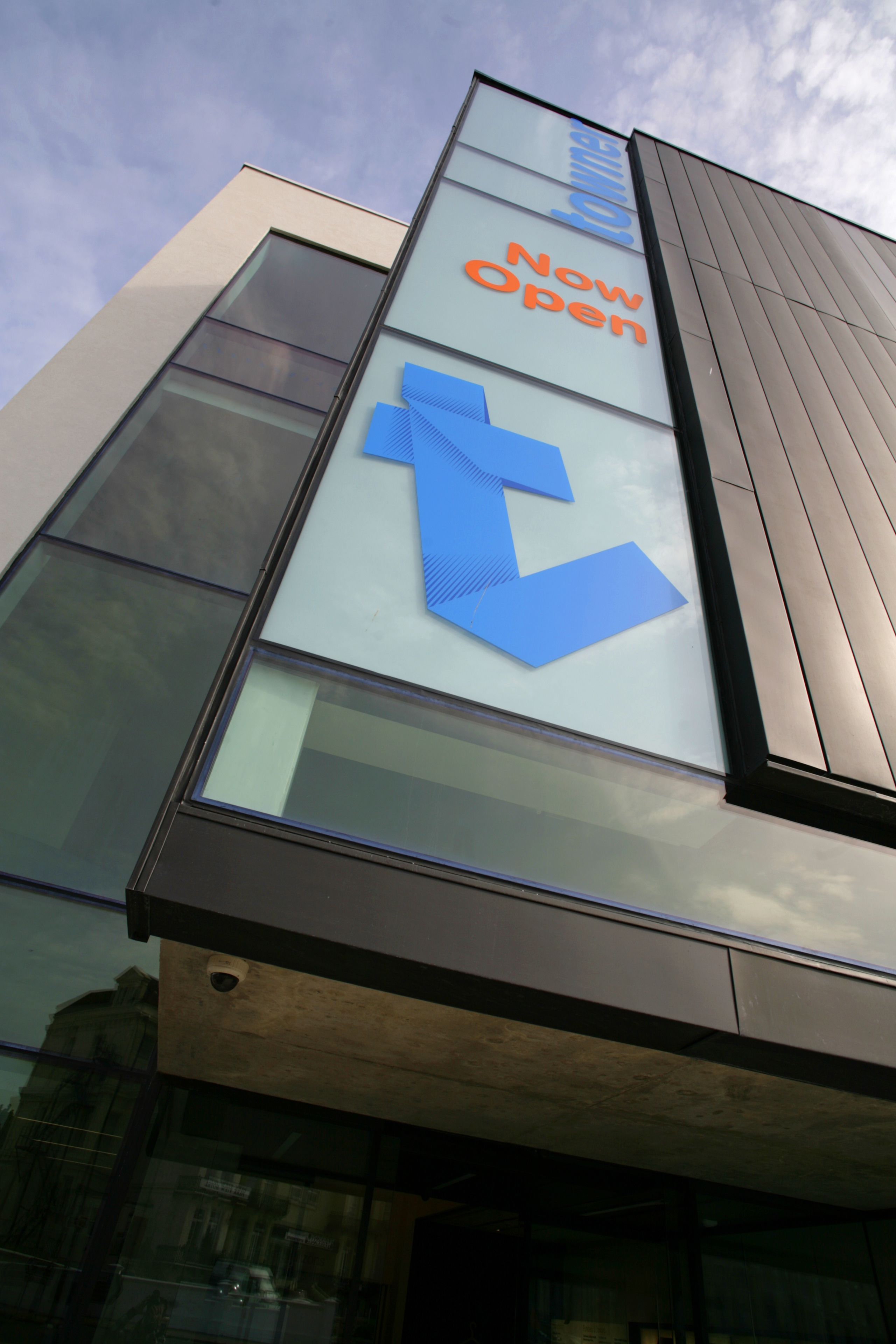 Een modern gebouw met een grote glazen gevel en een opvallend blauw pijl-bord dat een nieuwe opening aangeeft.
