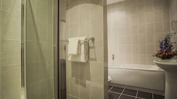 A modern bathroom with a glass shower enclosure, a white bathtub, and a sink with a vase of flowers.