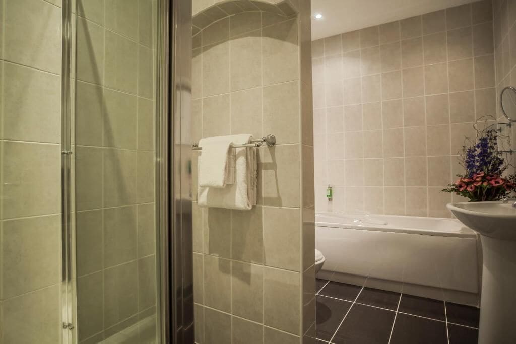 A bathroom with a glass shower enclosure, a bathtub, and a sink with a vase of flowers.