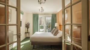 Ein Hotelzimmer mit einem großen Bett, einer Kandelaberleuchte, einem Vorhangfenster und einem Heizkörper.