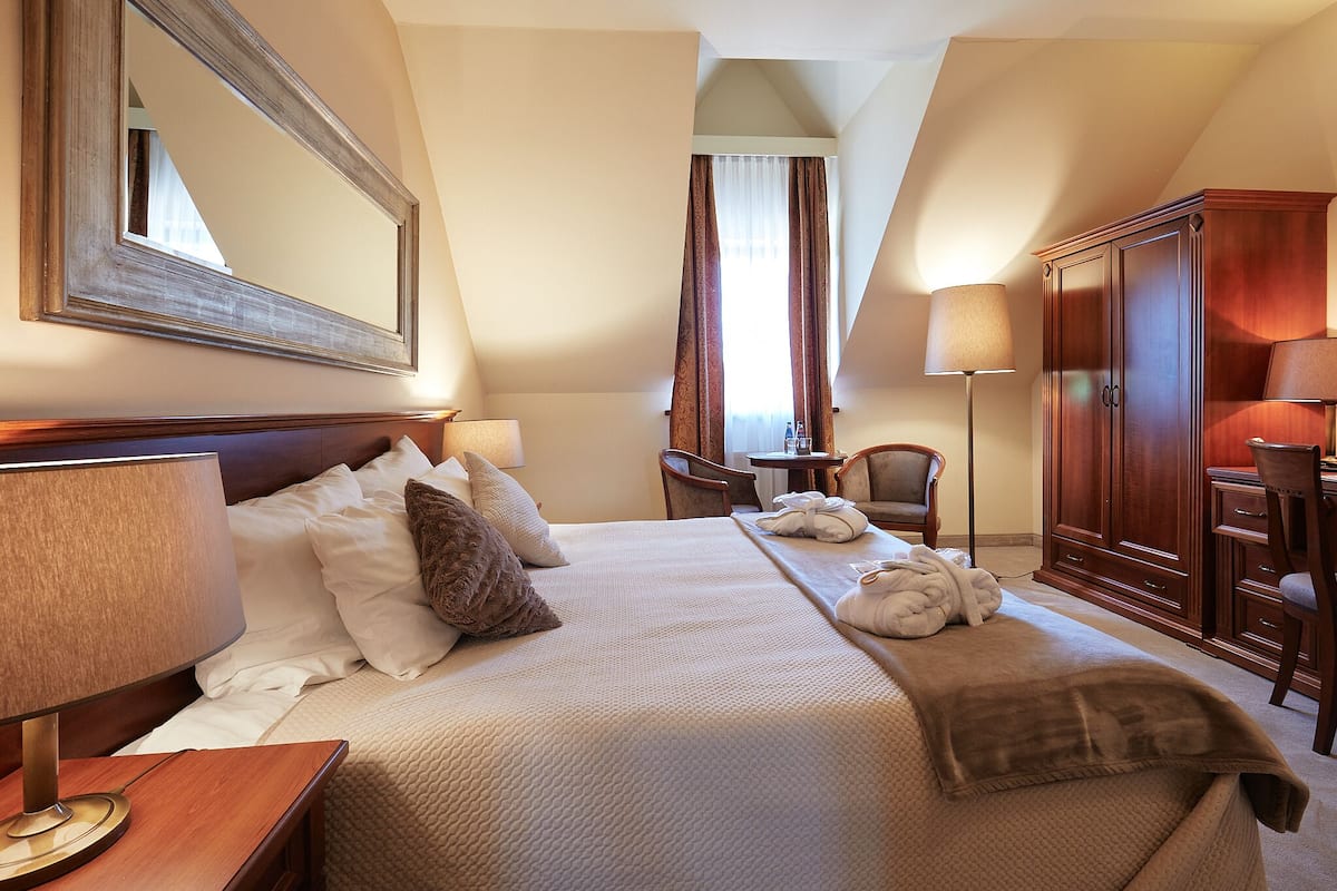 Ein Hotelzimmer mit einem großen Bett, einem Holzschrank, einem Schreibtisch mit Lampe und einem Sessel.