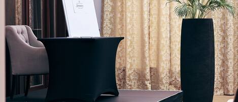 A stage with a presentation screen, a large black table, a tall black planter, and a patterned curtain.