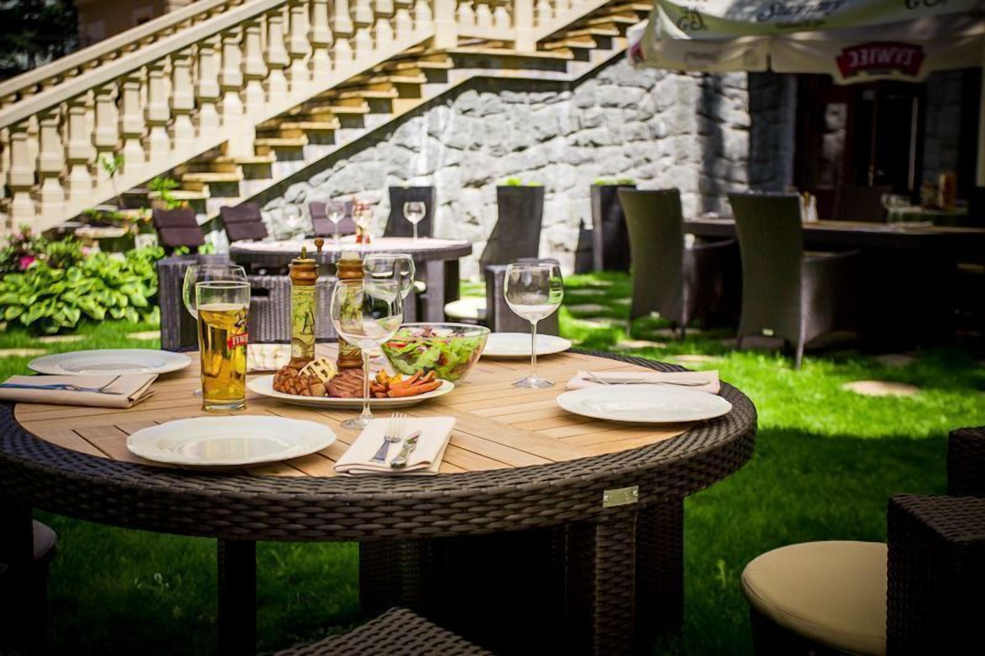 An outdoor dining area with wicker tables and chairs, a stone staircase, and a restaurant in the background.