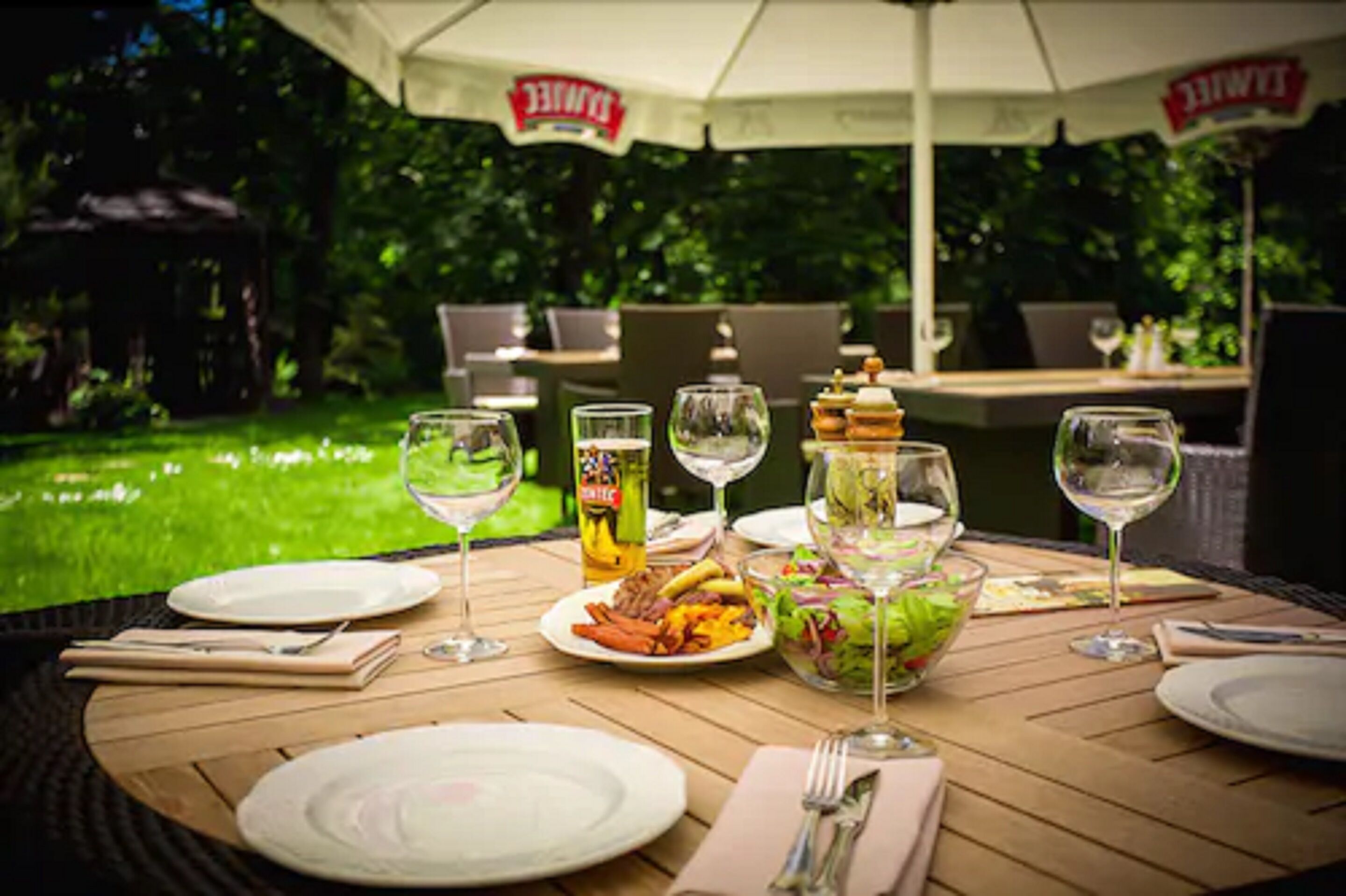 An outdoor dining area with a table set for a meal, surrounded by greenery.
