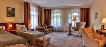 Quarto de hotel com duas camas, um sofá, uma cadeira e uma mesinha.