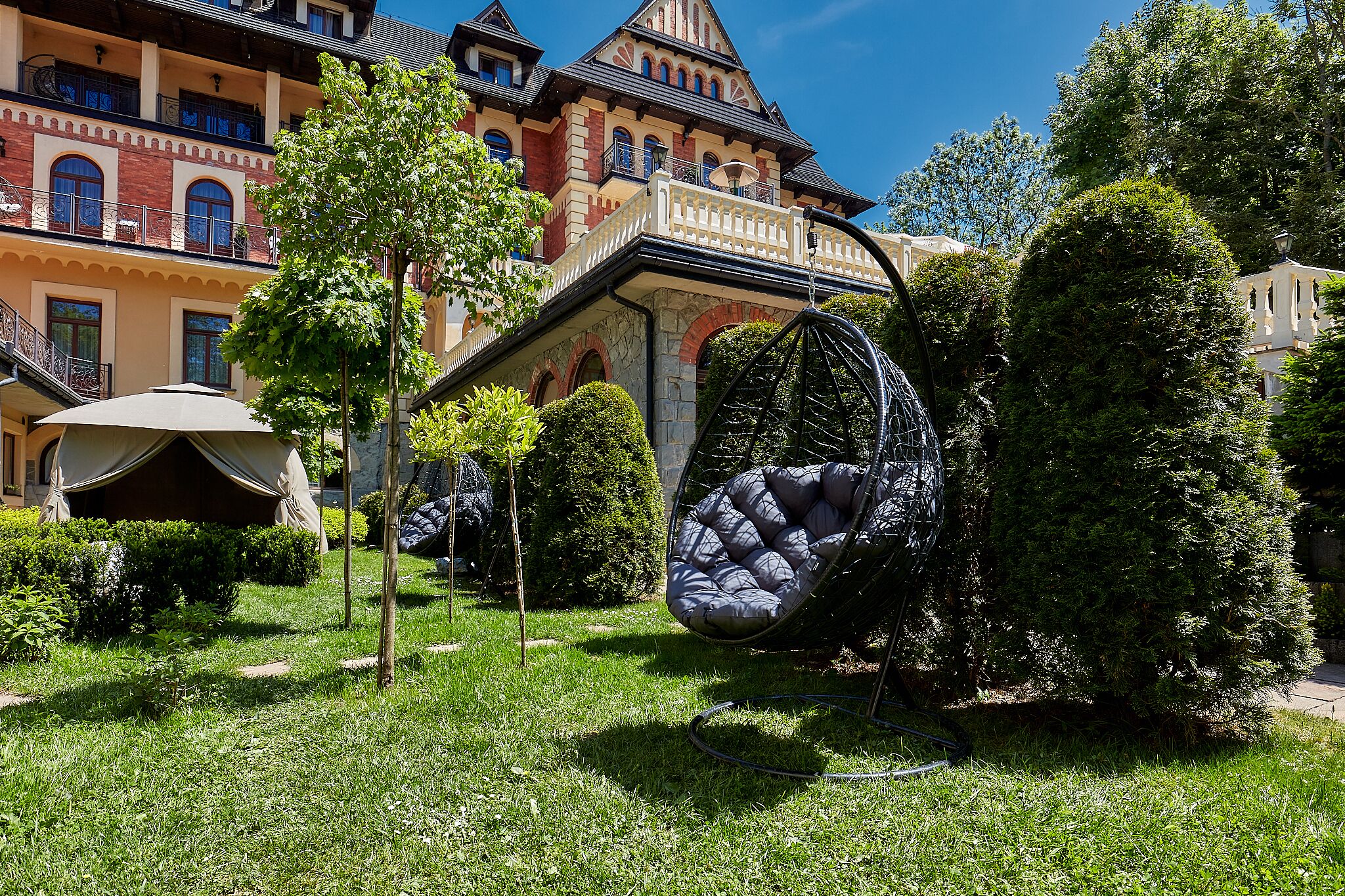 Un giardino con una sedia amaca, una tenda e un edificio con un balcone.