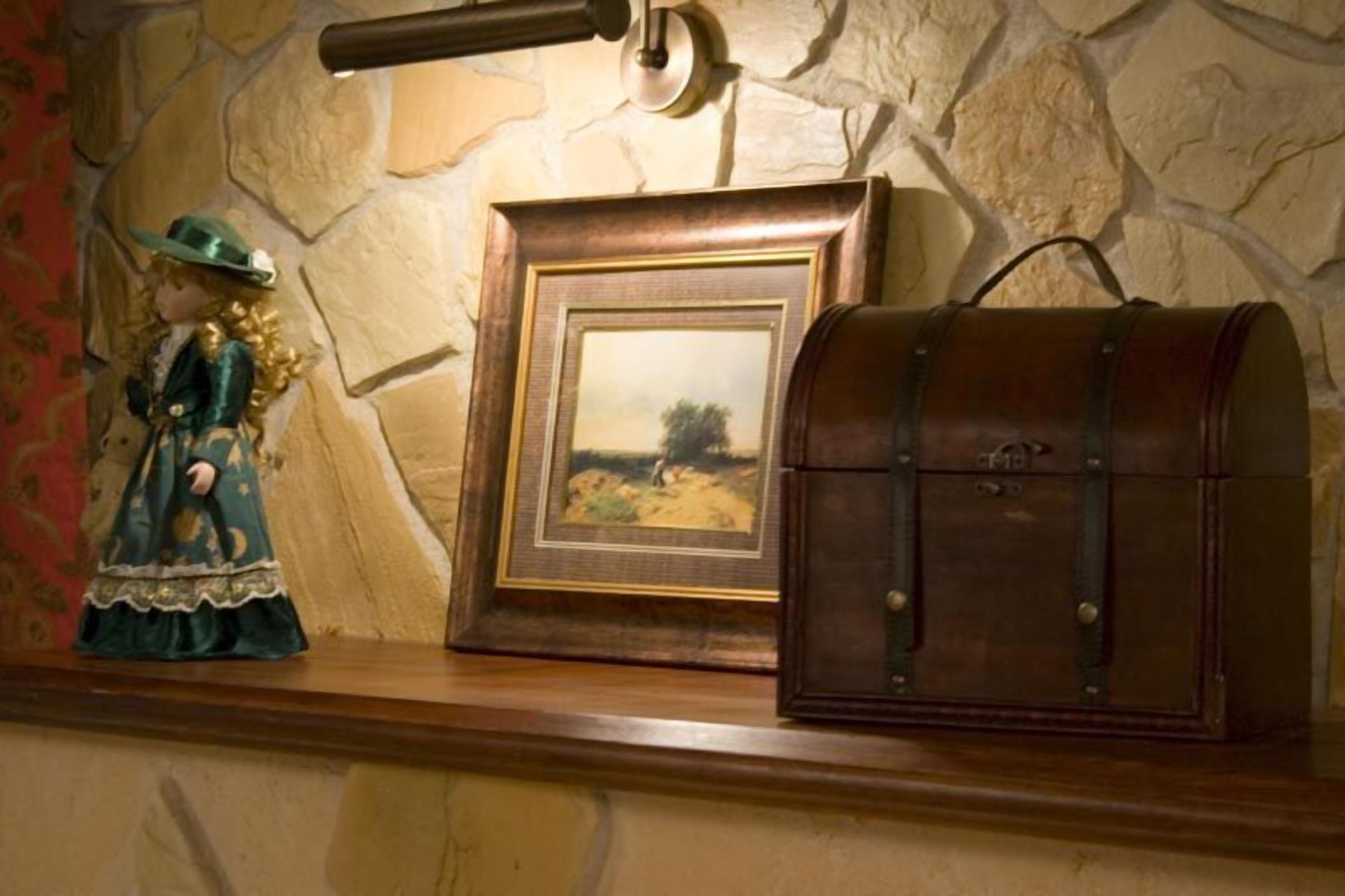 A wooden shelf with a framed landscape painting, a vintage-style leather satchel, and a doll dressed in a green outfit.