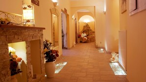 Pasillo de hotel con chimenea de piedra, arreglos florales y un letrero que indica el camino al baño.