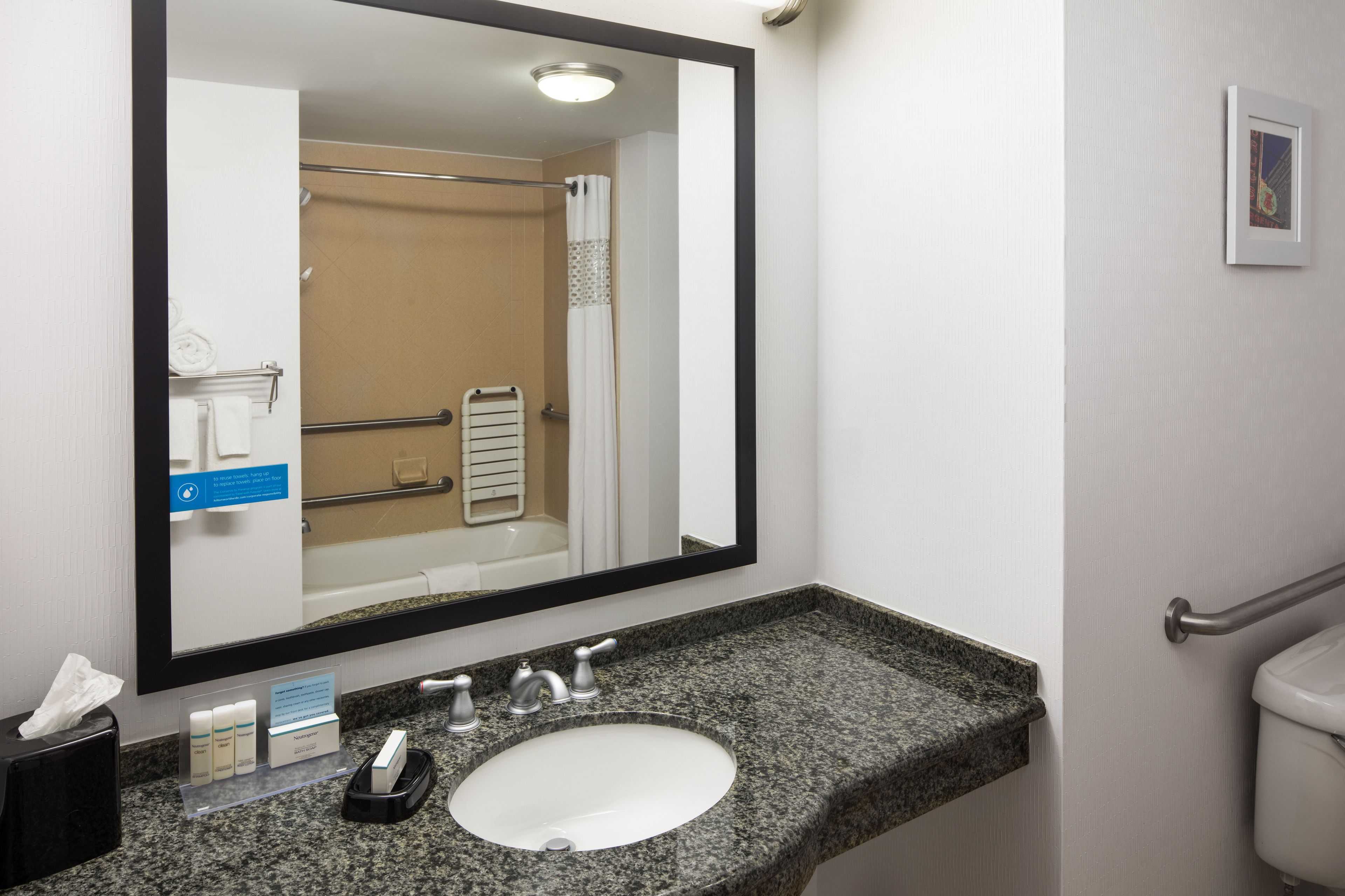 A bathroom with a granite countertop sink, a mirror, a towel rack, and a handrail.