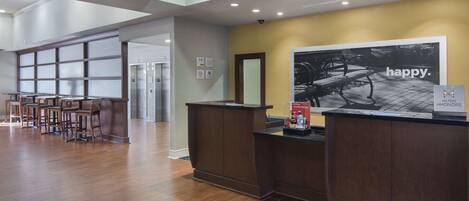 A reception area with a wooden reception desk, a large poster on the wall, and a bar area with stools.