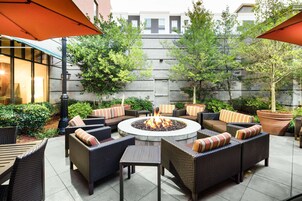 Un patio al aire libre con mobiliario de mimbre, una chimenea central y plantas en macetas.