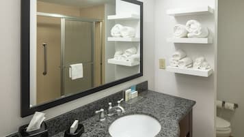 A bathroom with a granite countertop sink, a mirror, and white towel shelves.