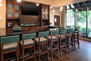 A bar area with wooden bar stools, a flat-screen TV mounted above the bar, and a large window offering a view of greenery outside.