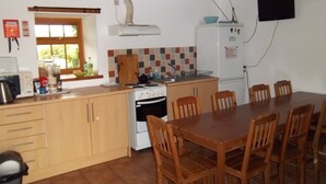 A compact kitchen with a stove, sink, and dining table with chairs. - Greencarts Bunkhouse (Hexham)