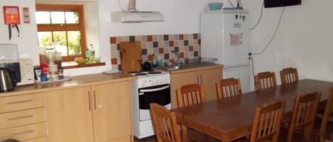 Cocina compacta con estufa, lavamanos y mesa de comedor con sillas.
