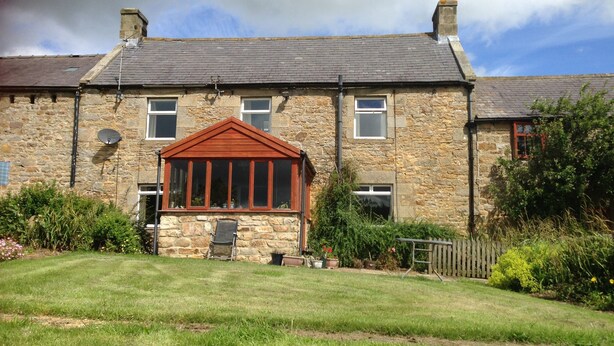 A stone house with a red front porch, a small garden, and a clear sky. - Greencarts Bunkhouse (Hexham)