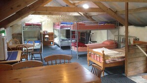 A dormitory room with bunk beds, a wooden table, chairs, and a bookshelf. - Greencarts Bunkhouse (Hexham)