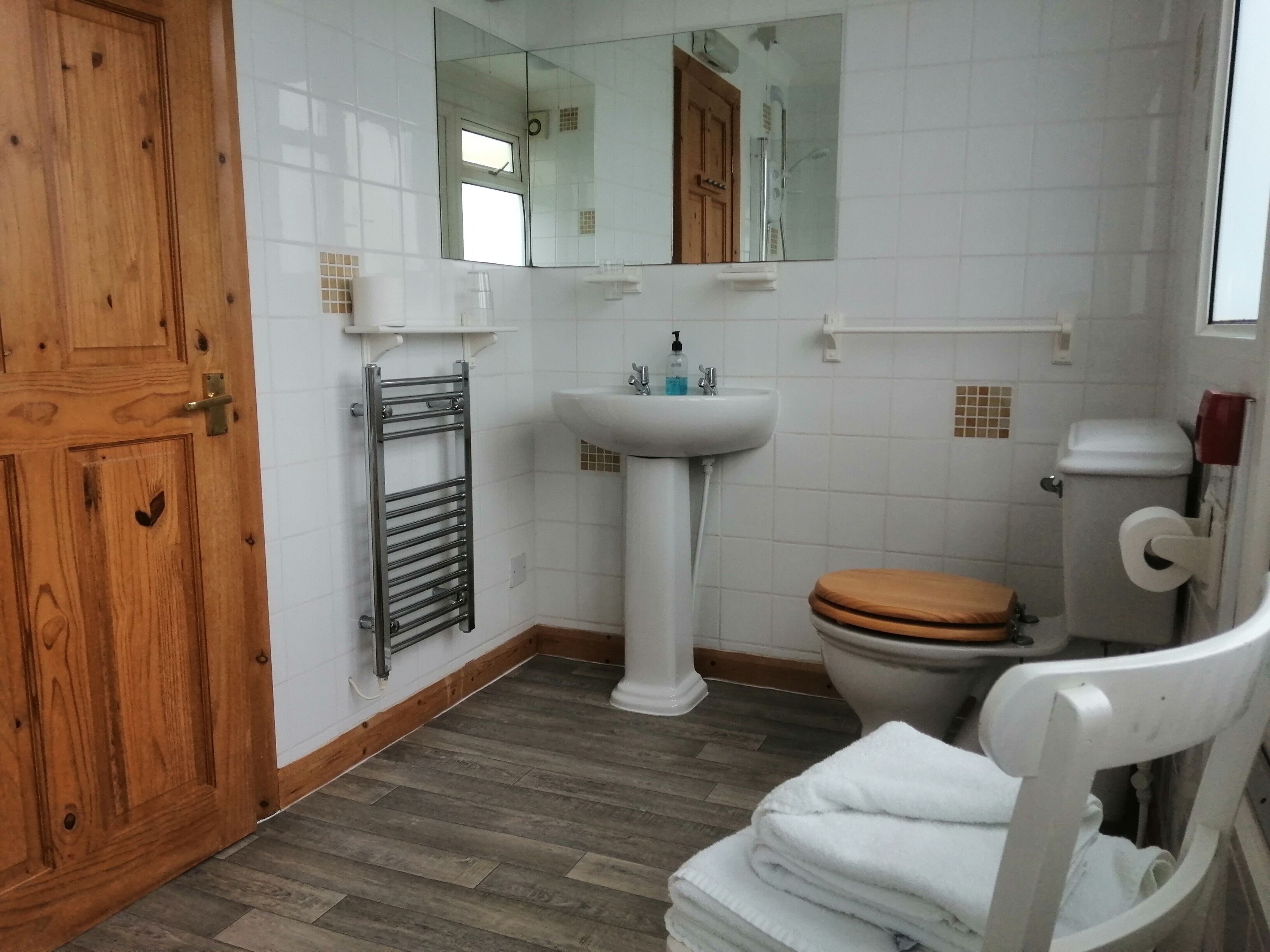 Une salle de bain avec une porte en bois, un lavabo blanc, des toilettes, un miroir et un porte-serviettes.